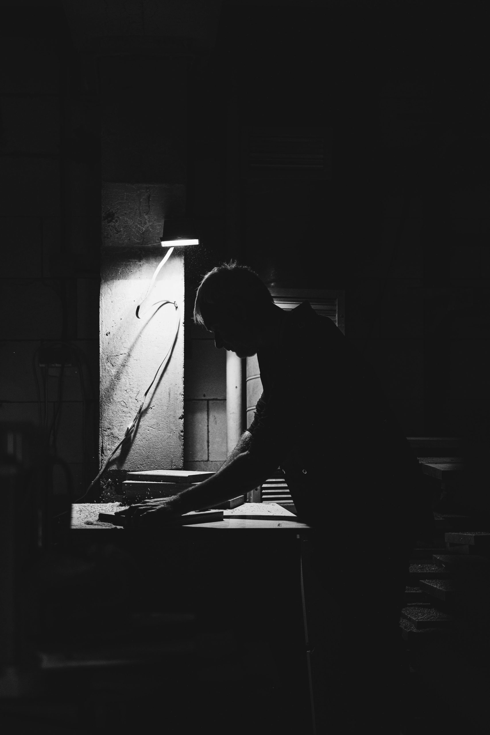 Black and white side view of anonymous male master standing at router table while shaping wooden detail in professional joinery
